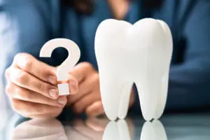 Image of man holding question mark next to a model tooth inquiring about Dental Malpractice Insurance questions.